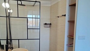 Ein modernes Badezimmer mit großem Spiegel, Waschtisch aus Holz, großem Topfbecken, Dusche mit Glastür und integriertem Ablagebereich.