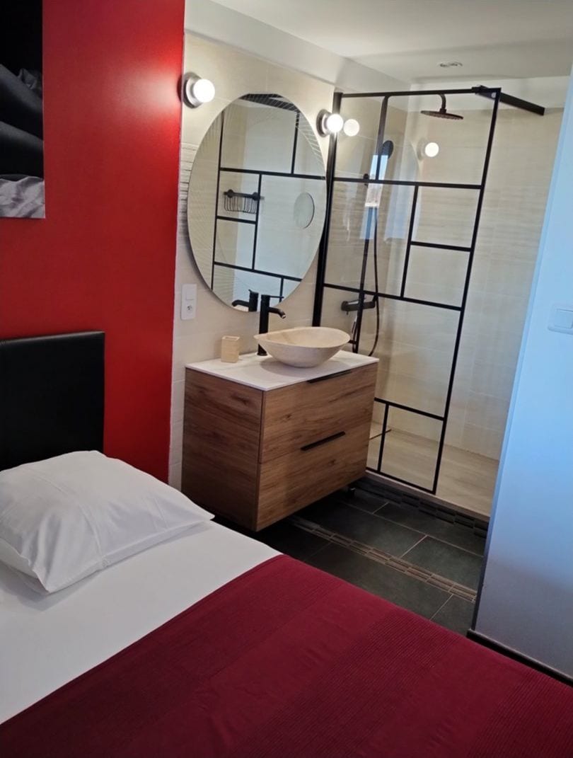 Un baño moderno con un espejo redondo, un tocador de madera y una cabina de ducha.