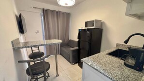 Una cocina compacta equipada con refrigerador, microondas, hervidor y un taburete pequeño.