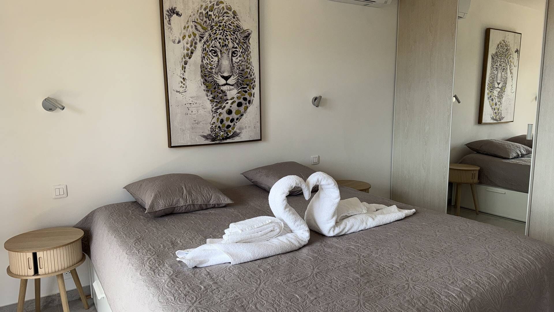 A bedroom with a bed, pillows, a mirror, and artwork on the wall.