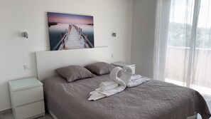 Ein Schlafzimmer mit einem Bett, zwei Nachttischen, einem Bild eines Piers und einem Fenster mit Vorhängen.