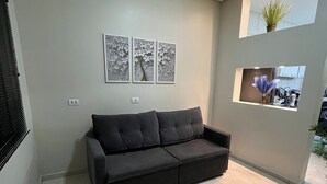 Un salón moderno con un sofá gris oscuro, suelo de baldosas y tres obras de arte colgadas en la pared que representan motivos florales.