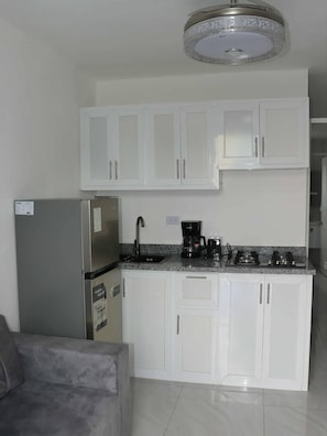 Una cocina con gabinetes blancos, un refrigerador de acero inoxidable, una cafetera y una estufa a gas.