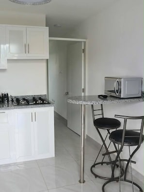 Una cocina con armarios blancos, estufa a gas, microondas y un taburete de bar.