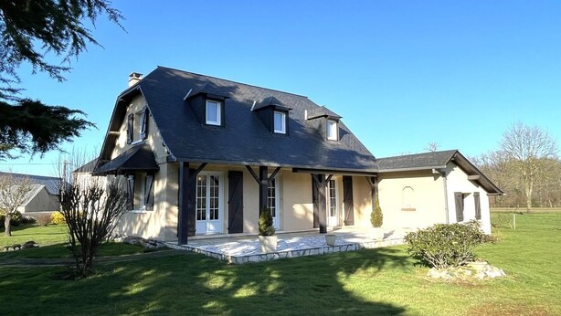 Ein zweistöckiges Haus mit dunklem Dach, einer Veranda und einem gepflegten Rasen.