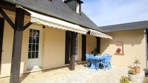 Eine überdachte Terrasse mit Steinboden, einem Tisch mit Stühlen und Kübelpflanzen.