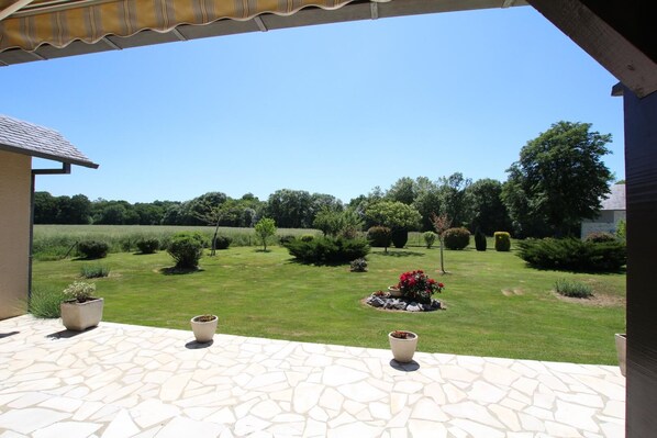 Une terrasse avec un sol en pierre, une vue sur un jardin bien entretenu et un ciel bleu dégagé.