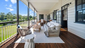 Un porche cubierto con muebles de mimbre, un sofá blanco y vistas a un paisaje verde.