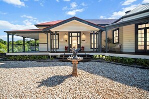 A modern house with a covered porch, a decorative bird fountain, and a gravel driveway. - Charming Queenslander With 5 Acres Private Land (Tamborine Mountain)