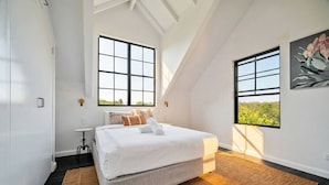 Un dormitorio moderno con una cama grande, dos ventanas y vistas a zonas verdes.