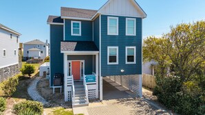 A two-story house with a front porch, a red door, and a sign indicating it is a Coastal Carolina property. - Rock Me on the Water: Oceanside, Pool, Hot Tub (Nags Head)