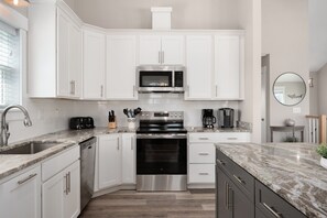 A modern kitchen with white cabinets, stainless steel appliances, a granite countertop, and a built-in oven. - Rock Me on the Water: Oceanside, Pool, Hot Tub (Nags Head)