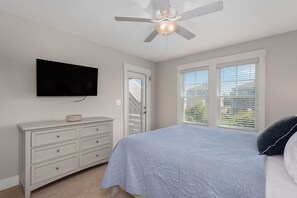 A bedroom with a bed, a dresser, a ceiling fan, a TV, and a window with blinds. - Rock Me on the Water: Oceanside, Pool, Hot Tub (Nags Head)