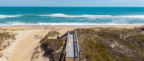 Una playa con un paseo marítimo de madera que lleva a la orilla, arena y olas del océano.