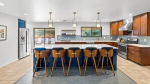 Une cuisine moderne dotée d’un îlot central, de tabourets de bar, d’appareils électroménagers en acier inoxydable et d’armoires en bois.