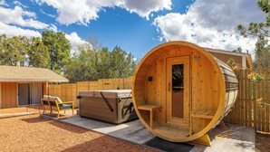 Un sauna en bois avec un banc à l’intérieur, un autre à l’extérieur, et un petit espace de détente extérieur avec une table et des chaises.