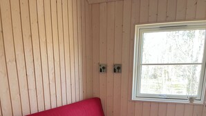 A red sofa in a room with wooden walls and a window.