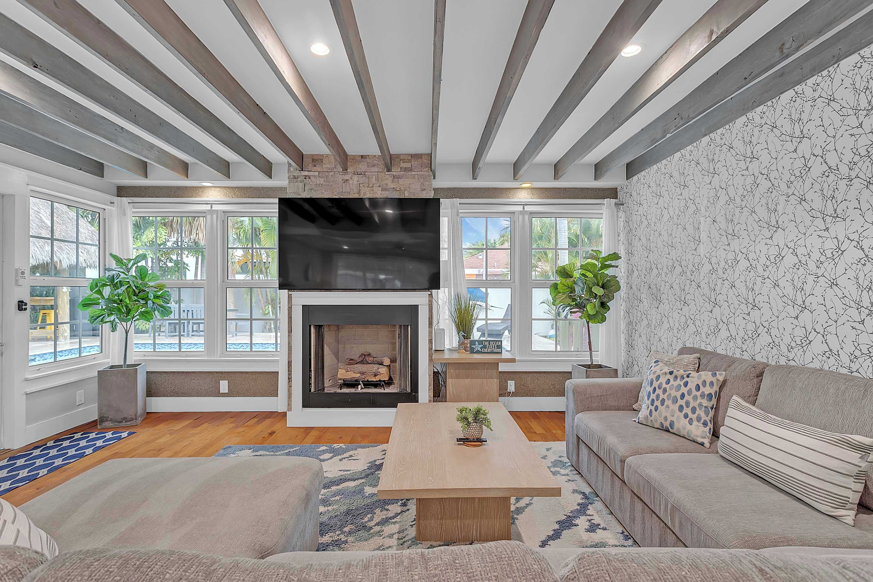 A living room with a fireplace, large windows, a flat-screen TV, and a sofa.