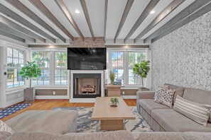 A living room with a fireplace, large windows, a flat-screen TV, and a sofa. - Tropical Oasis w/ Private Pool & Tiki Bar (Deerfield Beach)