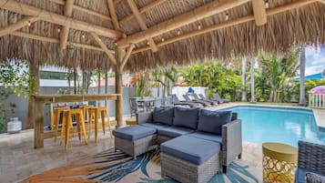 A covered outdoor area with a pool, wicker furniture, and a bar.