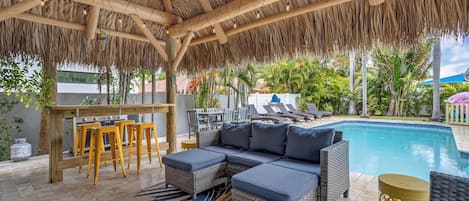 Un espace extérieur abrité comprenant une piscine, des meubles en osier et un bar.