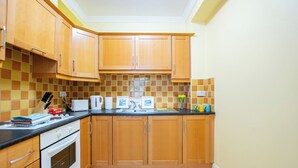 Une cuisine avec des meubles de rangement en bois, un pare-feu en carreaux, une cuisinière et divers appareils électroménagers.
