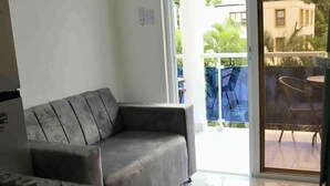 A modern kitchen with a gas stove, a grey sofa, and a sliding glass door leading to a balcony with outdoor furniture. - Condo Neuf 1 Chambre Sosua Près de Tout 306 (Sosúa)
