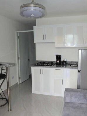 A compact kitchen with white cabinets, a granite countertop, a coffee maker, and a refrigerator. - Condo Neuf 1 Chambre Sosua Près de Tout 306 (Sosúa)