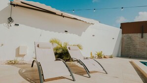 A modern outdoor lounge area with two reclining chairs, a small pool, and a white wall with a textured section. - Mary's Villas  (Oranjestad)