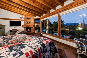 Ein Schlafzimmer mit einem großen Bett, einem Kamin, einem Fernseher und Blick auf Pool und Garten.