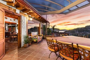 Ein Essbereich mit Blick auf einen Sonnenuntergang, Holzmöbel und eine Terrasse mit Topfpflanzen.