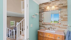 A bathroom with a stone wall, a sink, and a mirror. - Beautiful Large Waterfront Retreat W/ Heated Pool And Lanai!☀️ (Merritt Island)