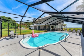 An indoor swimming pool with a flamingo float, surrounded by chairs and a covered area.