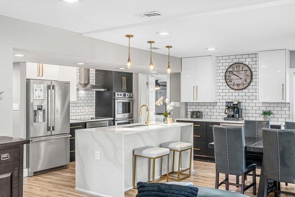 A modern kitchen with a central island, stainless steel appliances, and pendant lighting. - Perfect Group Getaway W/ Heated Saltwater Pool, Screened Porch & Patio! 🌅 (Merritt Island)