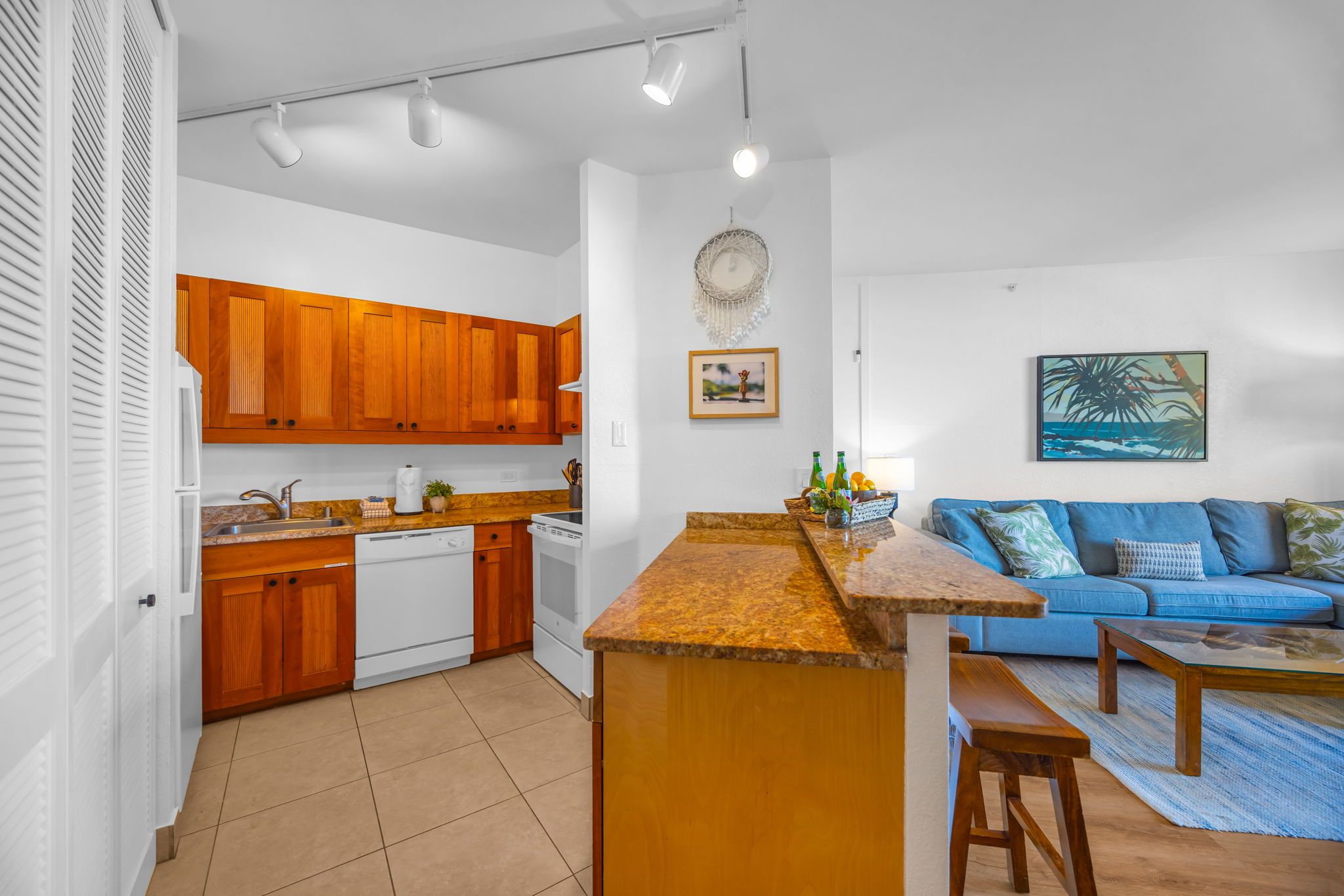 A modern kitchen with wooden cabinets, a central island, and a blue sofa in the living area.