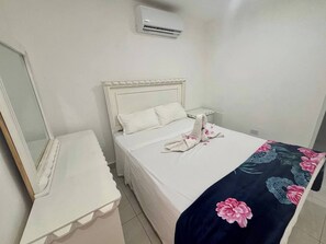 A hotel room with a bed, a bedside table, a mirror, and an air conditioning unit. - Condo, Neuf, Balcon en Plein Coeur de Sosua 204 (Sosúa)