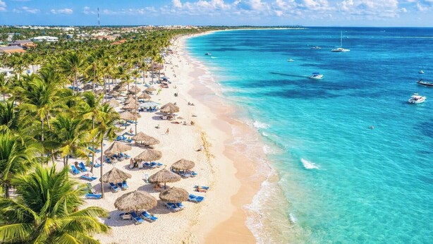 Ein Strand mit klarem türkisblauem Wasser, Palmen und Strandsonnenschirmen.