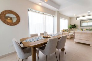 A modern living room with a wooden dining table, grey upholstered chairs, a floral sofa, and a round mirror on the wall. - Modern Poolside Villa in Vistacana Near Downtown (Punta Cana)