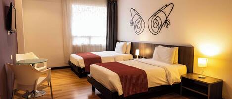 Una habitación de hotel con dos camas, una mesita pequeña, una silla, una mesita de noche con lámpara y una obra de arte en la pared.
