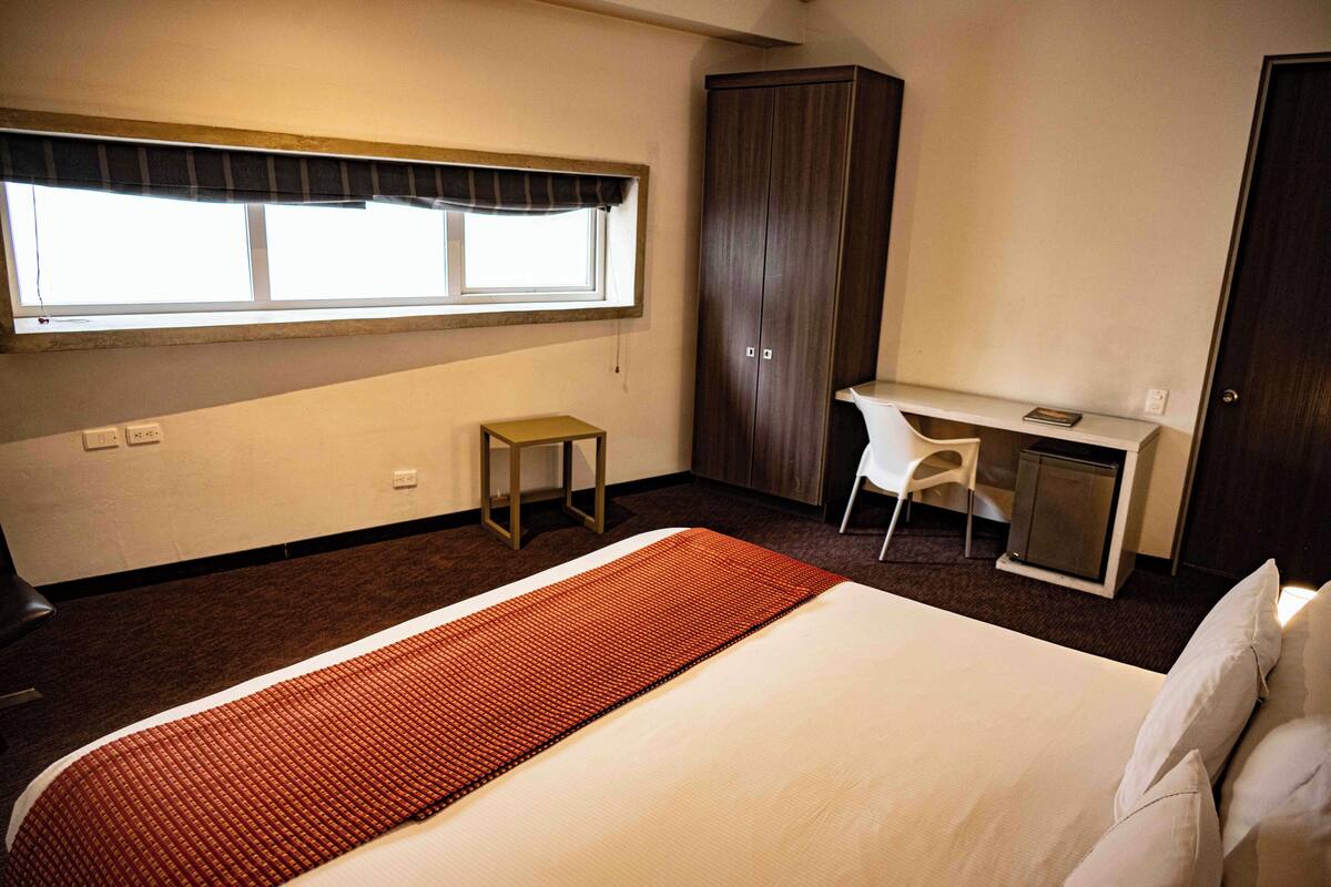 Ein Hotelzimmer mit Bett, Schreibtisch, Kleiderschrank und Fenster.