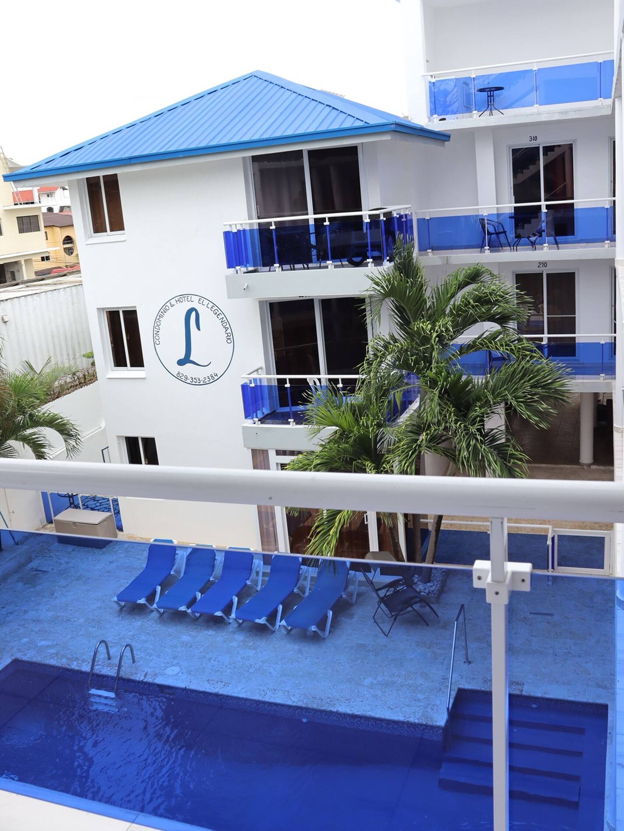 A hotel with a pool, blue lounge chairs, and a palm tree.