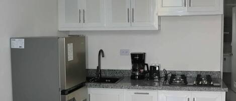 A kitchen with white cabinets, a stainless steel refrigerator, a coffee maker, and a gas stove.