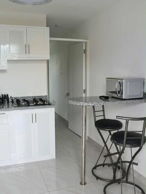 A kitchen with white cabinets, a gas stove, a microwave, and a bar stool. - Nouveau Codo à Sosua Près de Tout et Équipé, 405 (Sosúa)
