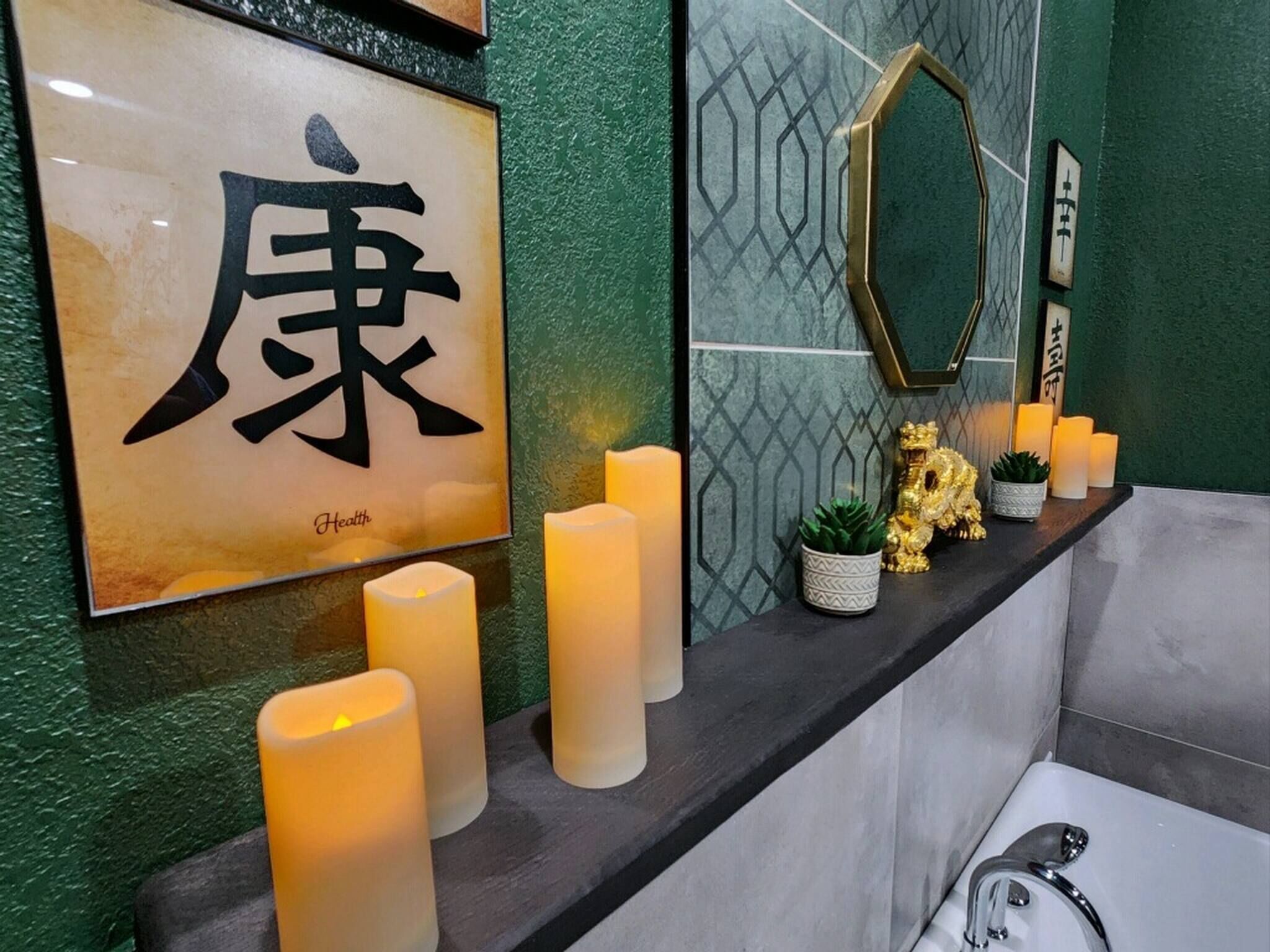 Ein Badezimmer mit einem großen, gerahmten chinesischen Schriftzeichen, Kerzen und dekorativen Pflanzen.