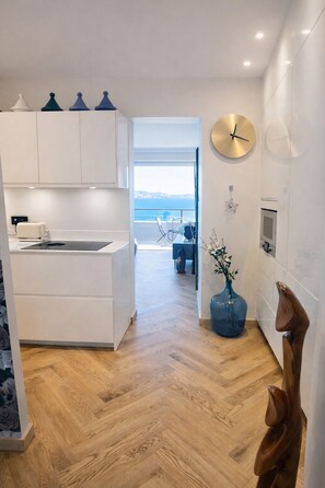 Eine moderne Küche mit weißen Schränken, Holzboden und Blick auf das Meer durch eine offene Tür.