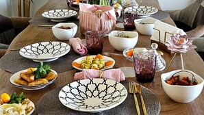 Taula de dinar posta amb diferents plats, un vas amb flors i un plat decoratiu a la paret.
