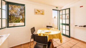 A dining area with a table set for two, chairs, a window with a view of trees, and a door leading outside. - Ideal retreat for couples or small families (Fuseta)