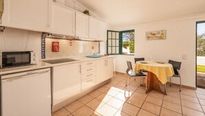 A kitchen with white cabinets, a microwave, and a dining area with a table and chairs. - Ideal retreat for couples or small families (Fuseta)