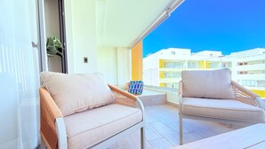 Ein Balkon mit zwei gepolsterten Stühlen und einem Holztisch mit Blick auf ein Wohngebiet mit modernen Gebäuden.