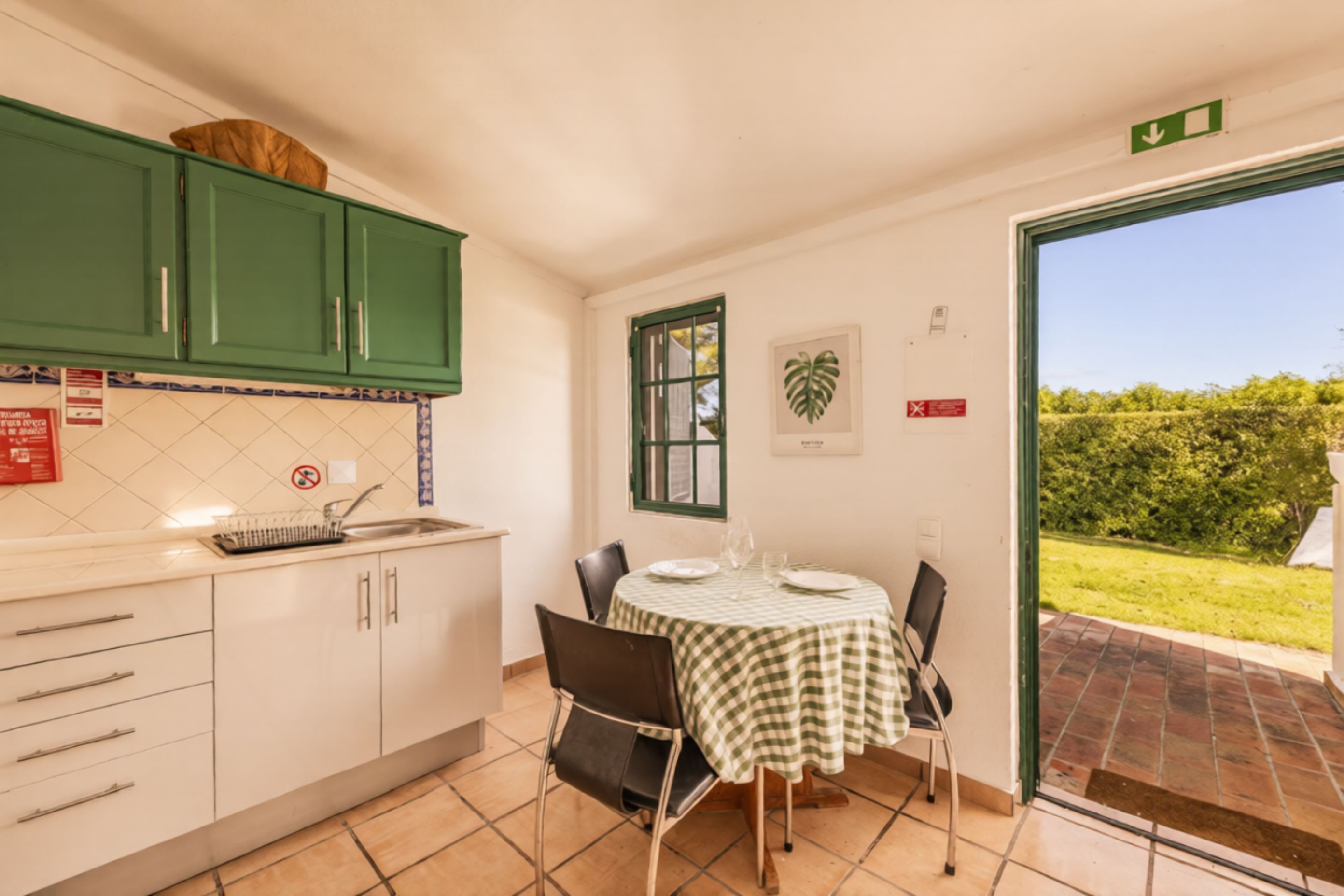 A kitchen with white cabinets, a dining table with chairs, and a view of a garden through an open door.